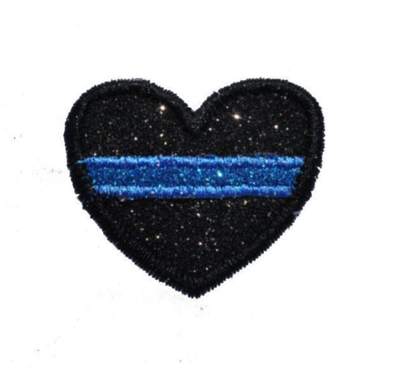 May include: Black heart-shaped patch with a thin blue stripe across the center. The patch is covered in glitter.