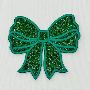 May include: A green glitter bow with a dark green outline. The bow is a decorative embellishment for crafts and projects.