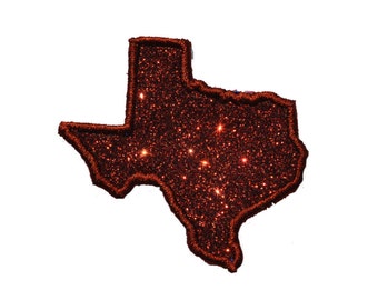 Puede incluir: Un contorno brillante del estado de Texas en purpurina marrón.