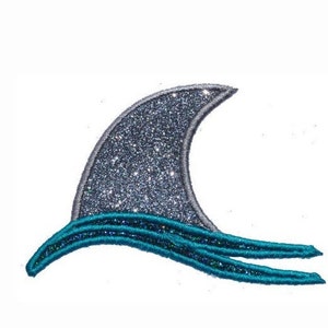 May include: A sparkly silver shark fin with a turquoise wave design.