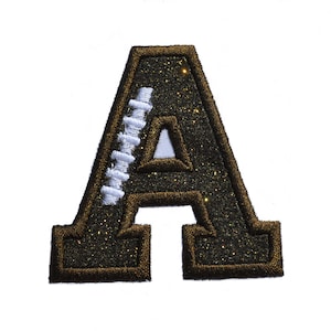 May include: A brown glitter letter A with a white stitched football design. The letter is a patch or iron-on.
