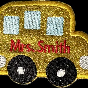 Könnte beinhalten: Ein goldener Glitzer-Schulbus mit dem Namen "Mrs. Smith", der in Rot gestickt ist. Der Bus hat weiße Fenster und schwarze Räder.