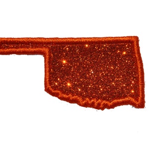 May include: Orange glitter iron-on patch in the shape of the state of Oklahoma.