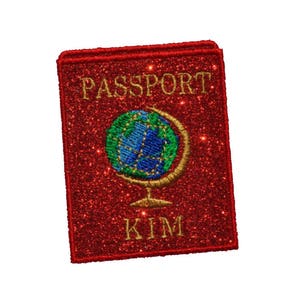 May include: A red glitter passport patch with gold lettering that reads "PASSPORT" and "KIM". The patch features an embroidered globe with blue and green continents. The patch is rectangular with rounded corners.