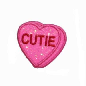 May include: Pink heart-shaped candy with glitter and the word "CUTIE" in red embroidery.