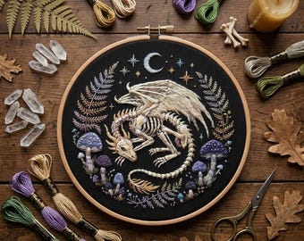 May include: An embroidered dragon skeleton design on a black background, set in a wooden embroidery hoop. The artwork features a crescent moon, stars, and mushrooms. Embroidery floss, crystals, and scissors surround the hoop on a wooden surface.