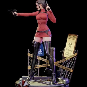 以下が含まれることがあります： 赤いドレスと黒いブーツを着て、2丁の銃を持っている女性の精巧なフィギュア。フィギュアは、バイオハザード警告サインとアンブレラ社のロゴが付いたプラットフォームに立っています。「BIOHAZARD WARNING」の文字が見えます。