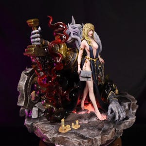 May include: A detailed fantasy figurine featuring a woman in a flowing black dress and a golden crown, standing next to a large armored figure with a hammer. The base is a rocky surface with candles.