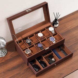 May include: A brown leather watch box with a glass top, showcasing various wristwatches with different band styles and face designs. The box has two levels, with a drawer containing accessories.