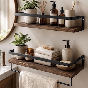 May include: Two wall-mounted shelves featuring dark brown wooden planks and matte black metal railings. The top shelf holds a speckled planter, reed diffuser, amber glass bottles, and a toothbrush holder. The bottom shelf includes a towel bar.