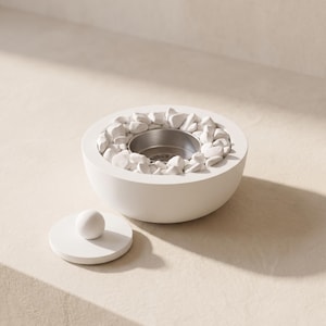 May include: A round white concrete fire pit bowl filled with small white decorative stones and a central stainless steel fuel cup. A matching circular white lid with a small spherical handle is placed beside the bowl on the surface.