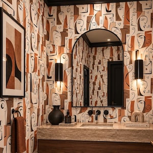May include: A bathroom interior featuring wallpaper with a repeating abstract face pattern in shades of brown, black, and white. The space includes a floating wooden vanity with a stone countertop, an arched mirror, and two black wall sconces.