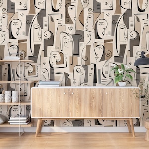 May include: Wallpaper featuring a repeating abstract pattern of stylized human faces in shades of beige, brown, gray, and black. The design consists of bold, continuous black lines forming facial features, interspersed with solid geometric shapes.