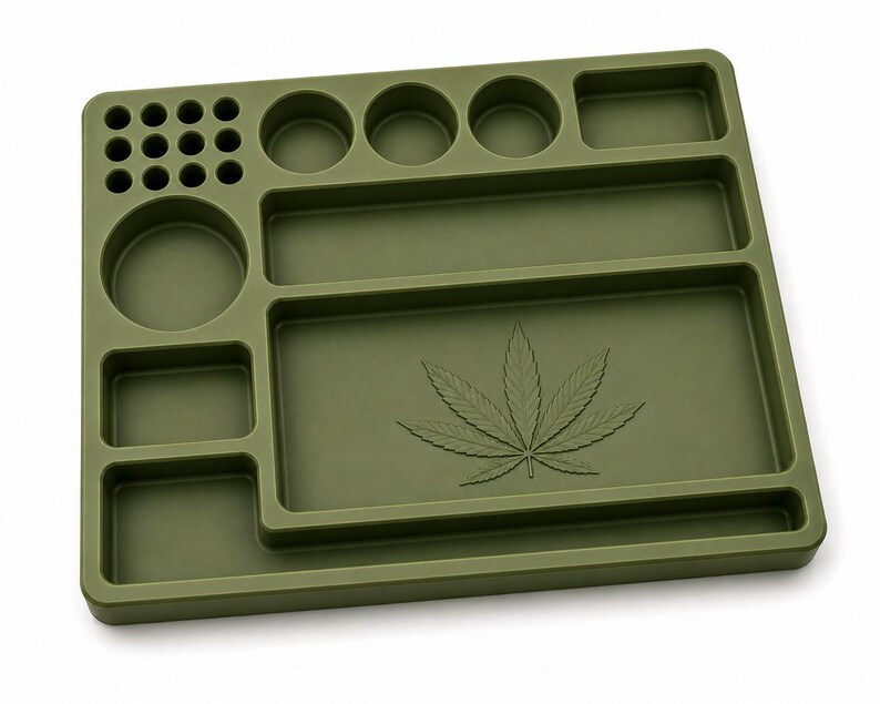 Puede incluir: Una bandeja para liar de color verde oliva con m&uacute;ltiples compartimentos y un dise&ntilde;o de hoja de cannabis. La bandeja presenta secciones circulares y rectangulares de varios tama&ntilde;os para almacenamiento y organizaci&oacute;n. La bandeja est&aacute; hecha de un material duradero.