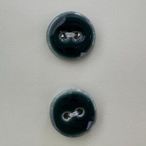 May include: Two dark green ceramic buttons with a white thread loop.