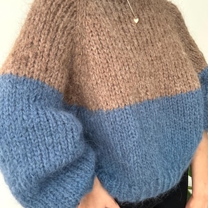 以下が含まれることがあります： 暖かくオーバーサイズのツーカラーセーター。上部は温かみのある茶色、下部の袖と胴体はソフトブルーです。セーターは丸いネックラインとリラックスしたフィット感で、カジュアルウェアに最適です。