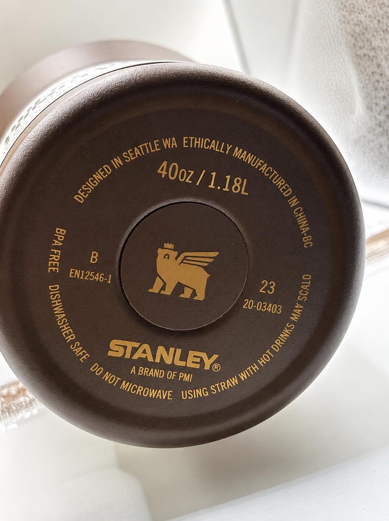 May include: Close-up of the bottom of a brown Stanley brand water bottle. The bottle is marked "40oz / 1.18L" and "Dishwasher Safe". The Stanley logo is visible, along with other text.