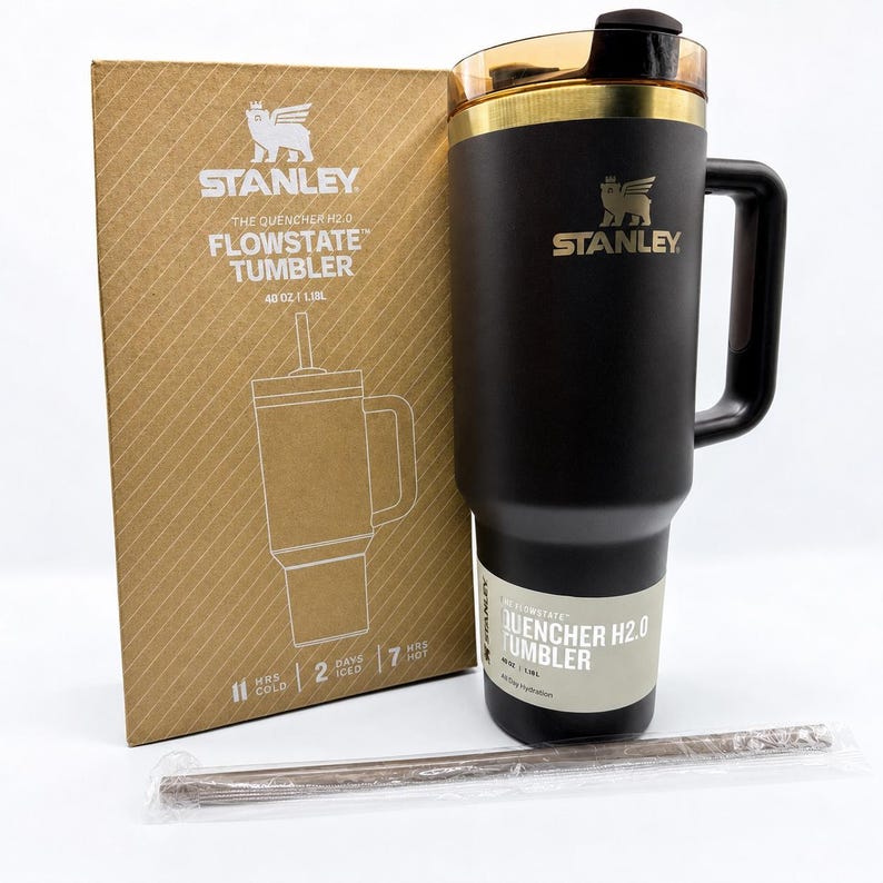 May include: Black Stanley Flowstate tumbler with a handle, gold accents, and a straw. The tumbler is 40 oz (1.18L) and comes with a cardboard box. The box and tumbler have the Stanley logo and text that reads "The Quencher H2.0 Flowstate Tumbler".