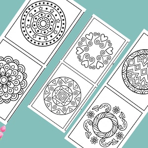 May include: A collection of coloring pages featuring intricate circular mandala designs in black and white. The pages are arranged on a light teal surface, with a bouquet of pink tulips and daisies in the corners.