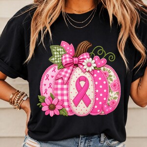 Puede incluir: Una camiseta negra con un gráfico grande de calabaza con varios patrones en tonos rosa y blanco. El diseño de la calabaza incluye un lazo rosa de concienciación, un lazo a cuadros, detalles florales, lunares y pequeñas formas de corazón.