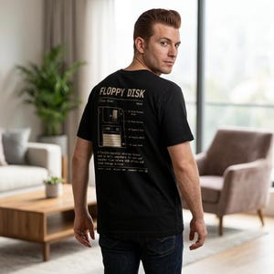 May include: Black t-shirt with a graphic of a floppy disk and the text "FLOPPY DISK" in a vintage style. The shirt includes a diagram and description of the floppy disk. The person is wearing blue jeans.