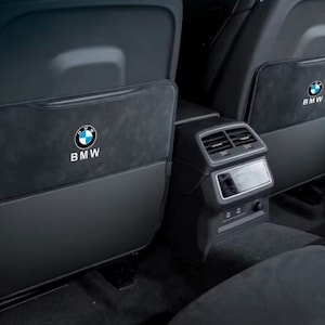 Pode incluir: Organizadores pretos para encosto de banco de carro com o logotipo da BMW em branco e azul. Os organizadores têm um bolso e são feitos de um material escuro e texturizado. O logotipo da BMW está centralizado.