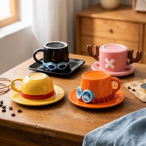 Op de afbeelding: Vier keramische koffiemokken met bijpassende schotels op een houten tafel. De mokken zijn geel, oranje, zwart en roze. Elke mok heeft een uniek ontwerp, waaronder een bril, een kruis en een strohoed.