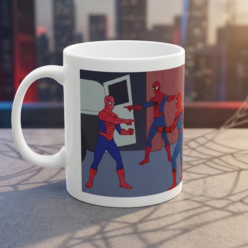 May include: White ceramic mug featuring the Spider-Man pointing meme. The meme depicts three Spider-Man characters pointing at each other in a room with a car door in the background. The mug has a curved handle.