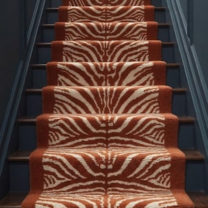 May include: A staircase runner featuring a repeating white zebra stripe pattern set against a deep terracotta orange background. The textured carpet covers the centre of each wooden stair tread, extending from the bottom step to the top landing.