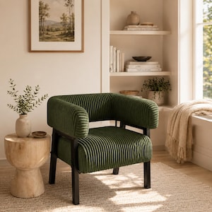 Puede incluir: Un sill&oacute;n de pana verde con estructura de metal negro. La silla tiene reposabrazos redondeados y una textura acanalada. La habitaci&oacute;n incluye una mesa auxiliar de madera y una pintura de paisaje enmarcada.