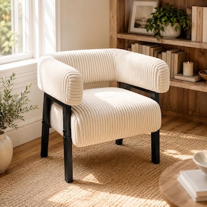 Puede incluir: Sill&oacute;n de pana color crema con estructura de metal negro. La silla tiene respaldo y reposabrazos redondeados. Se encuentra frente a una ventana, una estanter&iacute;a de madera y una alfombra de tonos neutros. El dise&ntilde;o es moderno y acogedor.