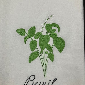 Peut inclure: Serviette de cuisine blanche avec une broderie d'un plant de basilic vert. Le basilic présente des feuilles vertes détaillées et de petites fleurs blanches. Le mot "Basil" est brodé en cursive en dessous.