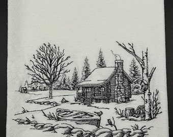 May include: White kitchen towel featuring a black embroidered design of a cabin in a snowy landscape. The design includes a cabin, trees, a boat, and rocks, creating a rustic, winter scene.