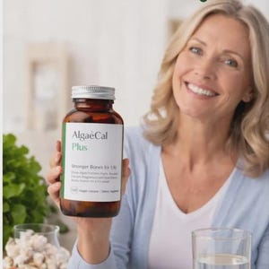 May include: A woman holding a brown bottle of AlgaeCal Plus, with the text "Stronger Bones Naturally" above. A glass of water and a bowl of fruit are on the table. The bottle label reads "Stronger Bones for Life".
