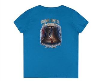 May include: A bright blue t-shirt featuring a graphic on the back of a bronze-coloured bell with a vertical crack. The text RUNG UNTIL IT BROKE appears above the bell, with 1776-2026 below it, set against a faded red, white, and blue flag background.