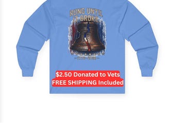 Puede incluir: Una camiseta de manga larga de color azul claro con un gráfico en la espalda de una campana de color bronce con una grieta en el centro. El texto RUNG UNTIL IT BROKE aparece sobre la campana, con 1776-2026 debajo, sobre un fondo rojo, blanco y azul.
