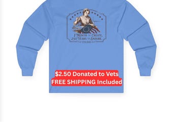 Puede incluir: Una camiseta de manga larga azul claro con un gráfico en la espalda de una persona cosiendo una bandera con estrellas en círculo. El texto dice: 1 MONTH TO CREATE, 250 YEARS TO ENDURE, 1776-2026. El diseño está enmarcado por un borde decorativo con estrellas.
