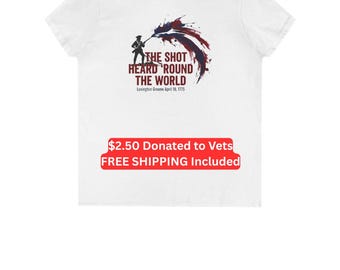Puede incluir: Una camiseta blanca de manga corta con un gráfico de un soldado con un mosquete y un efecto de salpicadura de pintura roja, blanca y azul. El texto dice: THE SHOT HEARD ROUND THE WORLD Lexington Greene April 19, 1775.