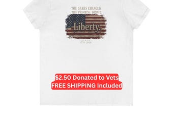 Puede incluir: Una camiseta blanca de manga corta con un gráfico en la parte posterior. El gráfico muestra una bandera estadounidense desgastada con el texto "THE STARS CHANGED. THE PROMISE DIDN'T." arriba, "Liberty." en el centro y "1776-2026" debajo.