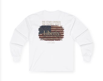 May include: A white long-sleeve shirt featuring a distressed American flag graphic on the back. The text reads THE STARS CHANGED. THE PROMISE DIDN'T. Liberty. 1776-2026. The design is centred on the back of the shirt with a weathered, vintage look.
