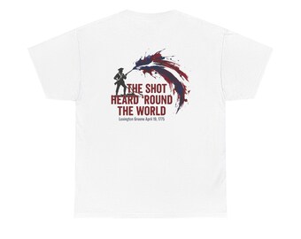 May include: A white t-shirt featuring a graphic of a soldier in silhouette with a red and blue paint splatter effect. The text reads THE SHOT HEARD 'ROUND THE WORLD and Lexington Greene April 19, 1775 in dark red and black lettering on the back.