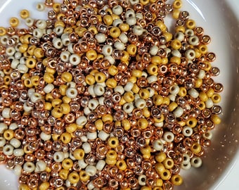 May include: A bowl filled with small, round beads in shades of cream, gold, and copper.