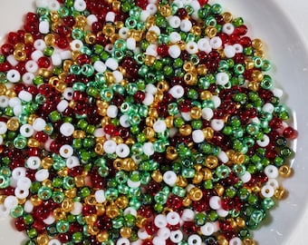 May include: A white plate filled with a variety of small, round beads in red, green, gold, and white colors.