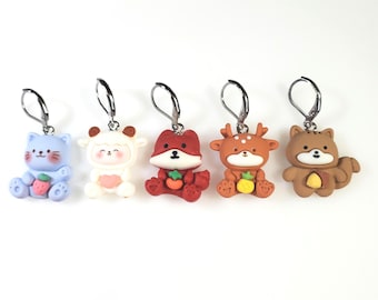 May include: Five colorful animal-shaped earrings. The earrings include a blue cat with strawberries, a white sheep, a red fox, a brown deer with a yellow fruit, and a brown bear with a yellow fruit. Each earring has a silver-colored hoop.