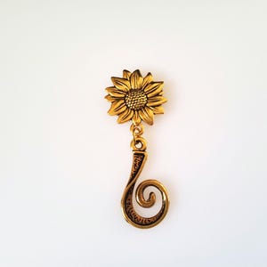 May include: Gold-toned sunflower charm with a curled stem. The sunflower has a detailed design and the stem is textured.