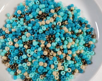 May include: A pile of small, round beads in shades of blue, turquoise, and cream. The beads are arranged in a random pattern, creating a visually appealing mix of colors.