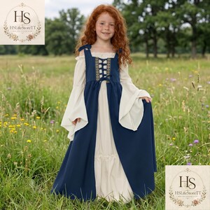 May include: A floor-length dress featuring a cream-coloured base with long, flowing sleeves and an off-the-shoulder neckline. A dark blue sleeveless over-tunic with a central lace-up bodice detail and gold-toned trim is layered over the dress.