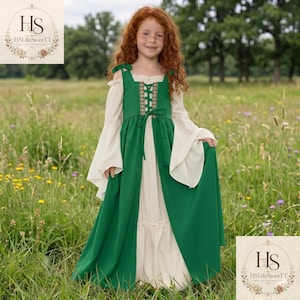 May include: A floor-length dress featuring a cream-coloured base with long, flared sleeves and an attached green over-layer. The green bodice includes a central lace-up detail with decorative trim, shoulder ties, and a full-length skirt design.