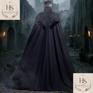 May include: A long, black cloak with a high collar and ornate shoulder detailing. The cloak is worn in a medieval setting, with a stone building and torches in the background. The cloak appears to be made of a heavy fabric.