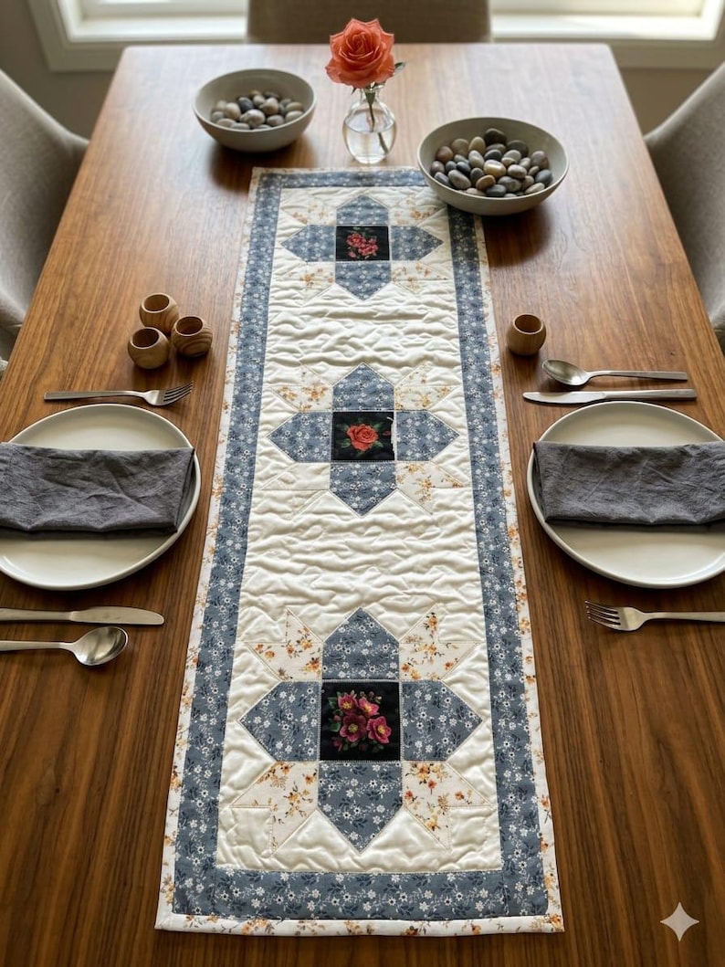 May include: A quilted table runner with a floral pattern and blue accents. The runner features a central design with a square of roses. The table is set with plates, silverware, and decorative bowls.